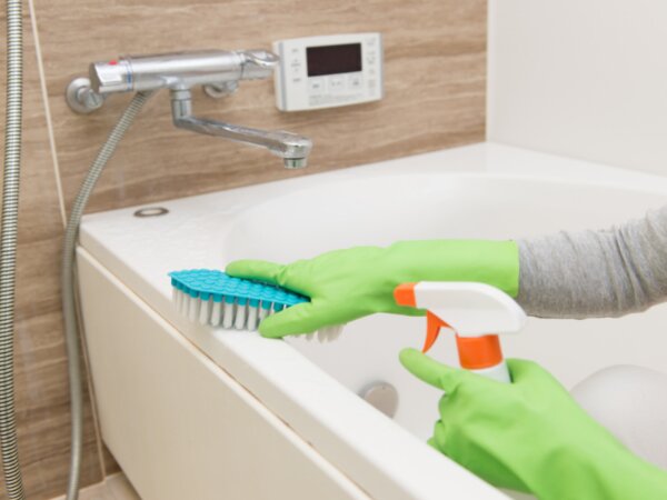 Putzen einer Badewanne mit Handschuhen und Bürste